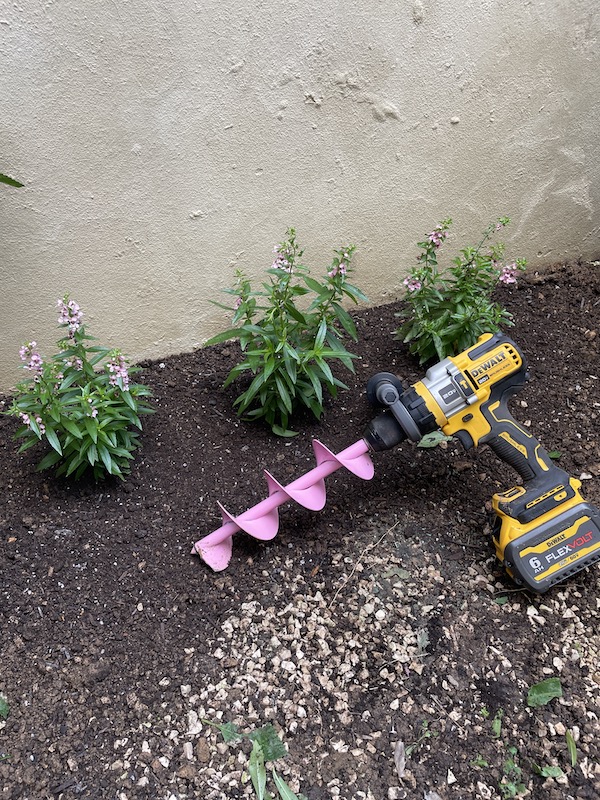 Plantas con flores rosadas junto a un taladro para el suelo en color rosado.